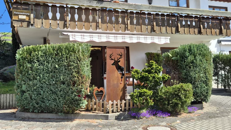 Außenaufnahme des Hauses mit grünen Hecken und Balkon der Ferienwohnung in Obermaiselstein.